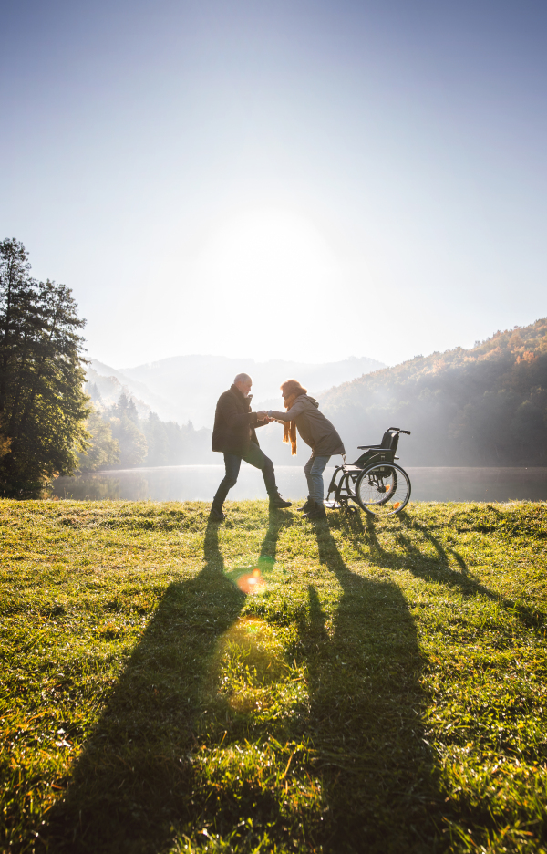 Active senior couple on a walk in a beautiful autumn nature. A man and woman in a wheelchair by the lake in the early morning.