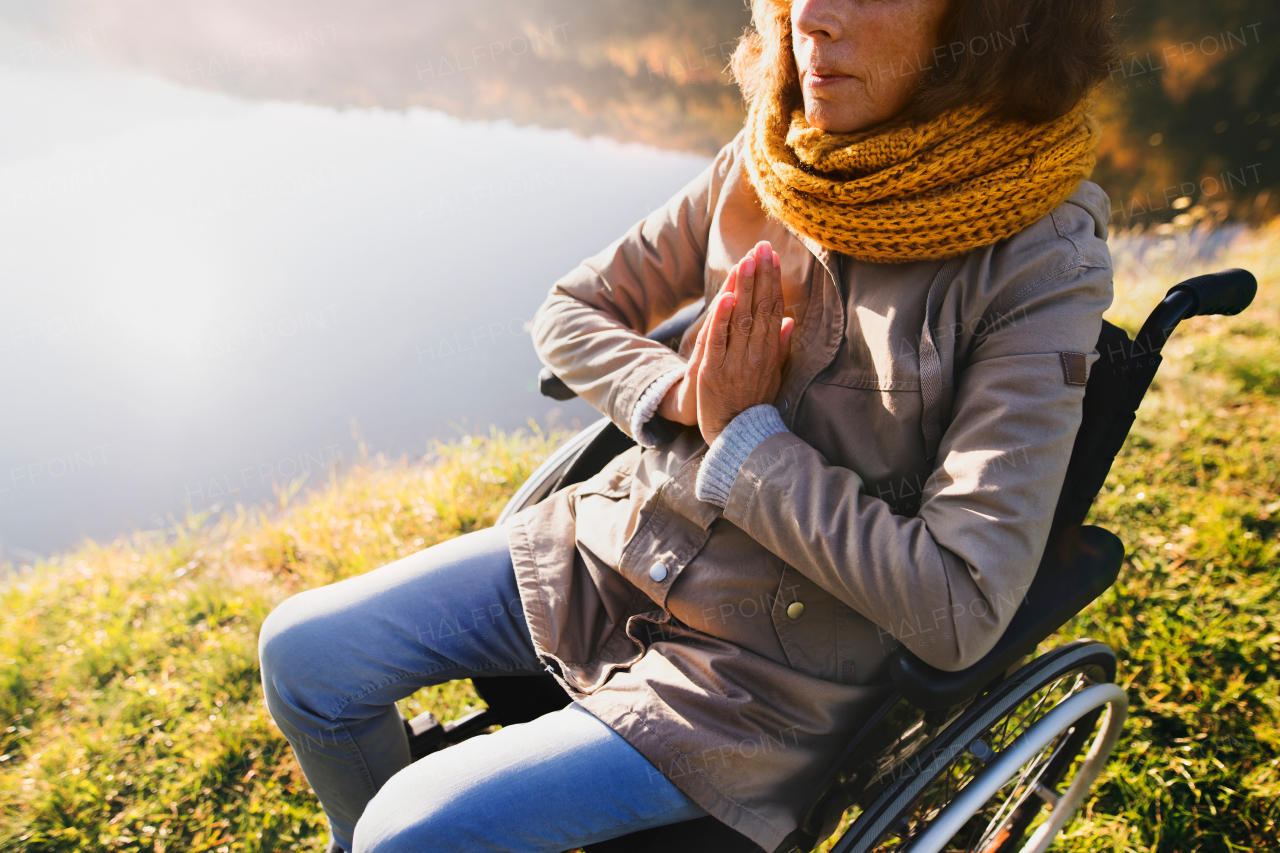 Unrecognizable senior woman in a wheelchair in an autumn nature. A woman praying by the lake in the early morning.