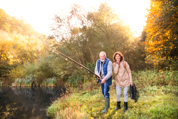 Active senior couple fishing at the lake. A woman and a man in a beautiful autumn nature in the early morning.