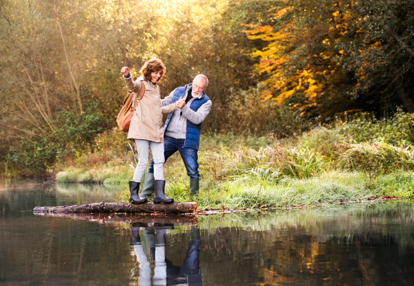 Active senior couple on a walk in a beautiful autumn nature. A woman and man by the lake in the early morning.