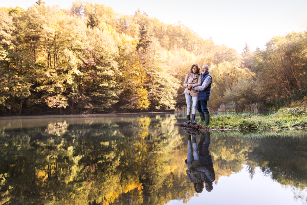 Active senior couple on a walk in a beautiful autumn nature. A woman and man by the lake in the early morning.