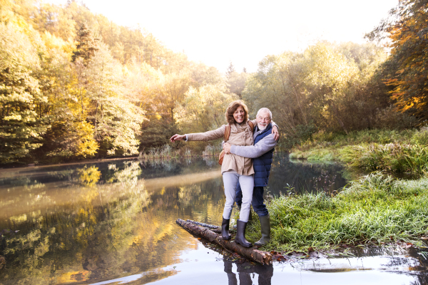 Active senior couple on a walk in a beautiful autumn nature. A woman and man by the lake in the early morning.