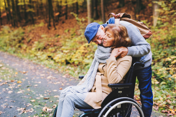 Active senior couple on a walk in a beautiful autumn nature. A man and woman in a wheelchair walking in forest.