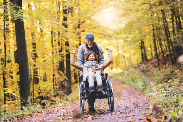 Active senior couple on a walk in a beautiful autumn nature. A man and woman in a wheelchair walking in forest.