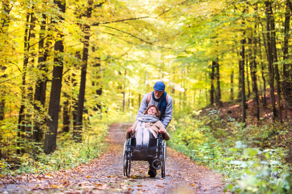 Active senior couple on a walk in a beautiful autumn nature. A man and woman in a wheelchair walking in forest.