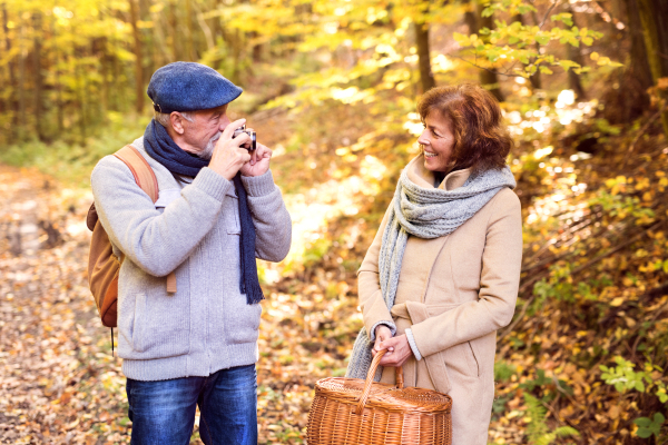 Active senior couple on a walk in a beautiful autumn nature. A man taking photograph with a camera.