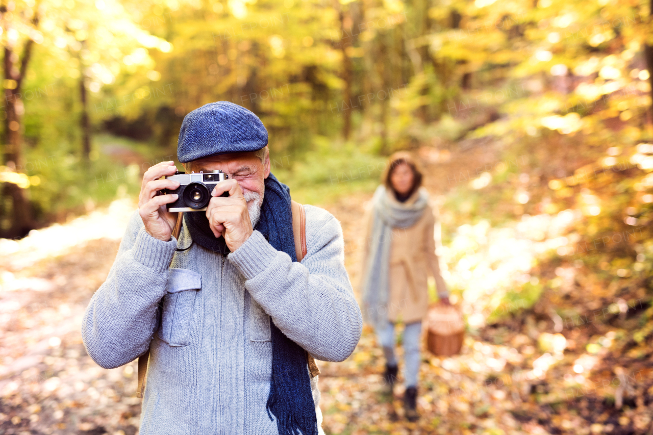 Active senior couple on a walk in a beautiful autumn nature. A man taking photograph with a camera.