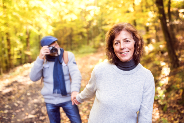 Active senior couple on a walk in a beautiful autumn nature. A man taking photograph with a camera.