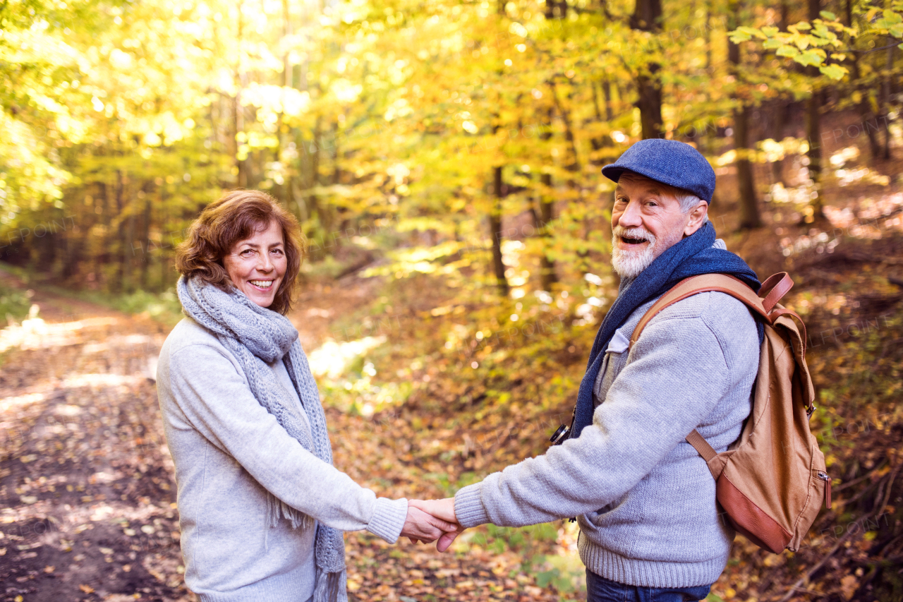 Active senior couple on a walk in a beautiful autumn nature. A man and woman holding hands.