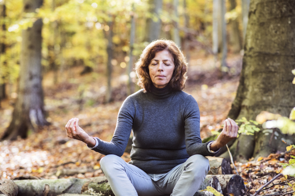 Senior woman meditating in an autumn forest. An old woman sitting on the ground, practicing yoga, eyes closed.