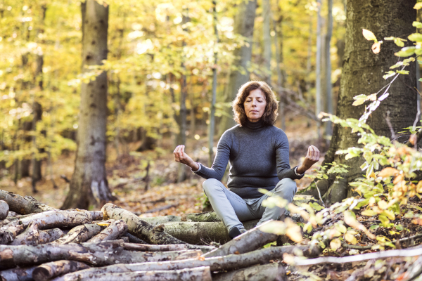 Senior woman meditating in an autumn forest. An old woman sitting on the ground, practicing yoga, eyes closed.