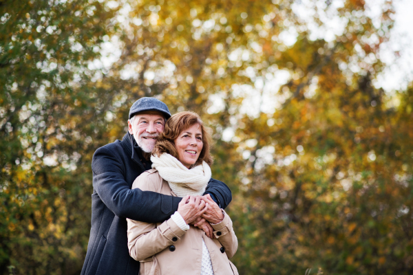 Active senior couple on a walk in a beautiful autumn nature. A man and woman standing and hugging. Copy space.