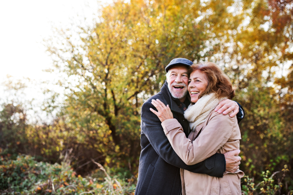 Active senior couple on a walk in a beautiful autumn nature. A man and woman standing and hugging. Copy space.