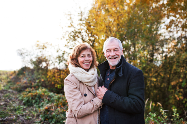 Active senior couple on a walk in a beautiful autumn nature. A man and woman standing and hugging.