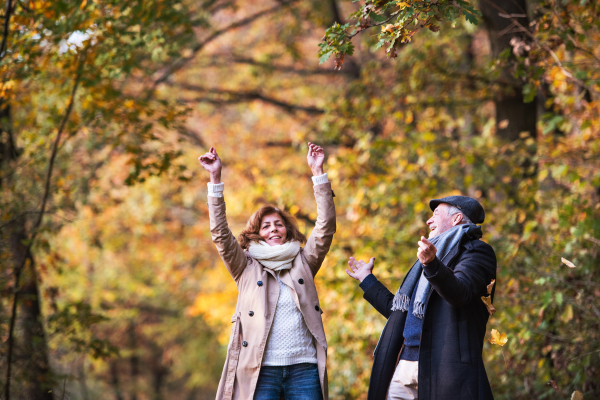 Happy senior couple on a walk in a forest in an autumn nature, having fun.