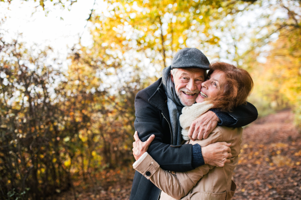 Active senior couple on a walk in a beautiful autumn nature. A man and woman standing and hugging. Copy space.