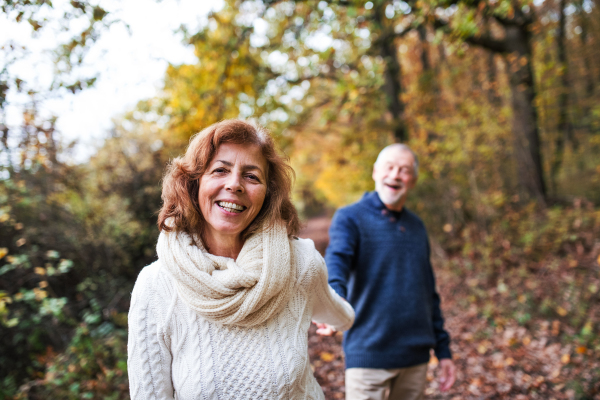 A portrait of an active senior couple walking in an autumn nature.