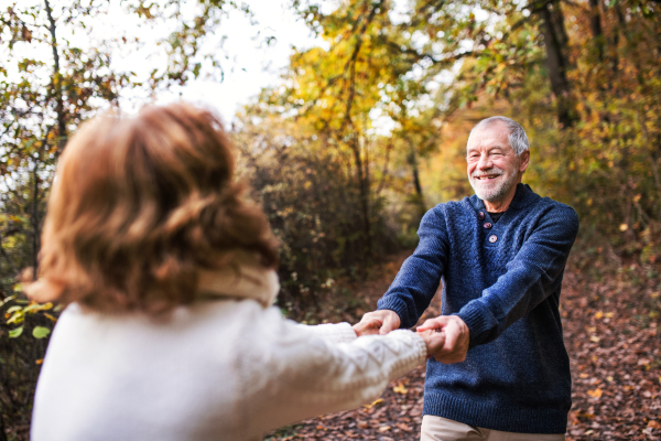 Senior couple looking at each other in an autumn nature, holding hands and spinning.