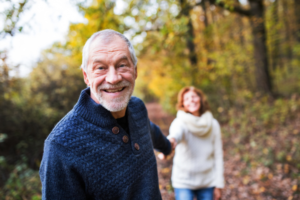 A portrait of an active senior couple walking in an autumn nature.