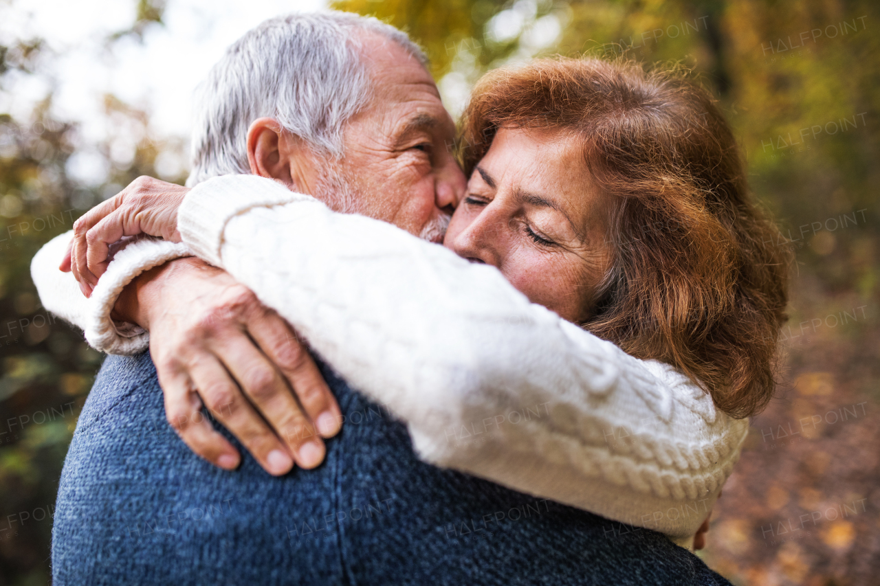 A close-up of an active senior couple on a walk in a beautiful autumn nature. A man and woman hugging and kissing.