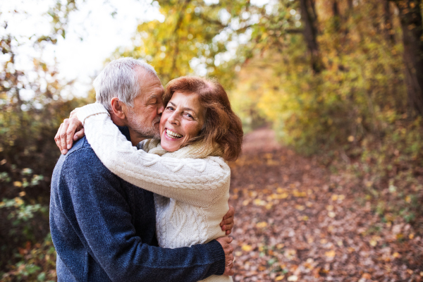 An active senior couple on a walk in a beautiful autumn nature. A man and woman hugging and kissing. Copy space.