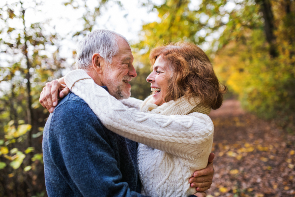 Active senior couple on a walk in a beautiful autumn nature. A man and woman looking at each other, hugging and laughing.