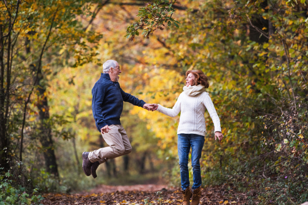 Senior couple looking at each other in an autumn nature, holding hands and jumping.