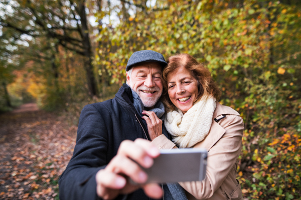 Active senior couple on a walk in a beautiful autumn nature, taking selfie. A man and woman in love, having good time.