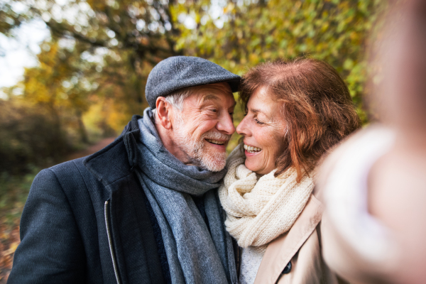 Active senior couple on a walk in a beautiful autumn nature, taking selfie. A man and woman in love, having good time.