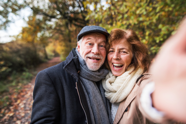 Active senior couple on a walk in a beautiful autumn nature, taking selfie. A man and woman in love, having good time.