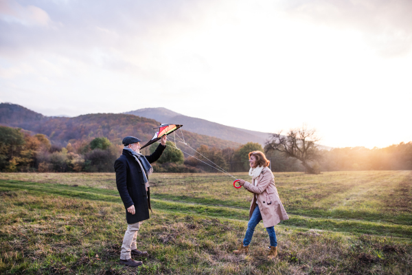 Carefree senior couple flying a kite in an autumn nature at sunset, laughing.