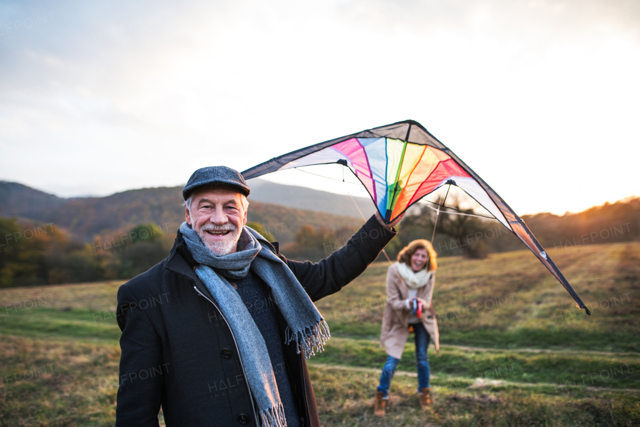 Carefree senior couple flying a kite in an autumn nature at sunset, laughing.