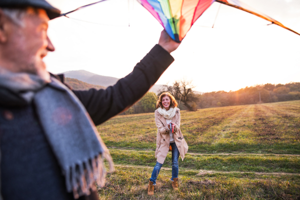 Carefree senior couple flying a kite in an autumn nature at sunset, laughing.