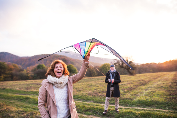 Carefree senior couple flying a kite in an autumn nature at sunset, laughing.