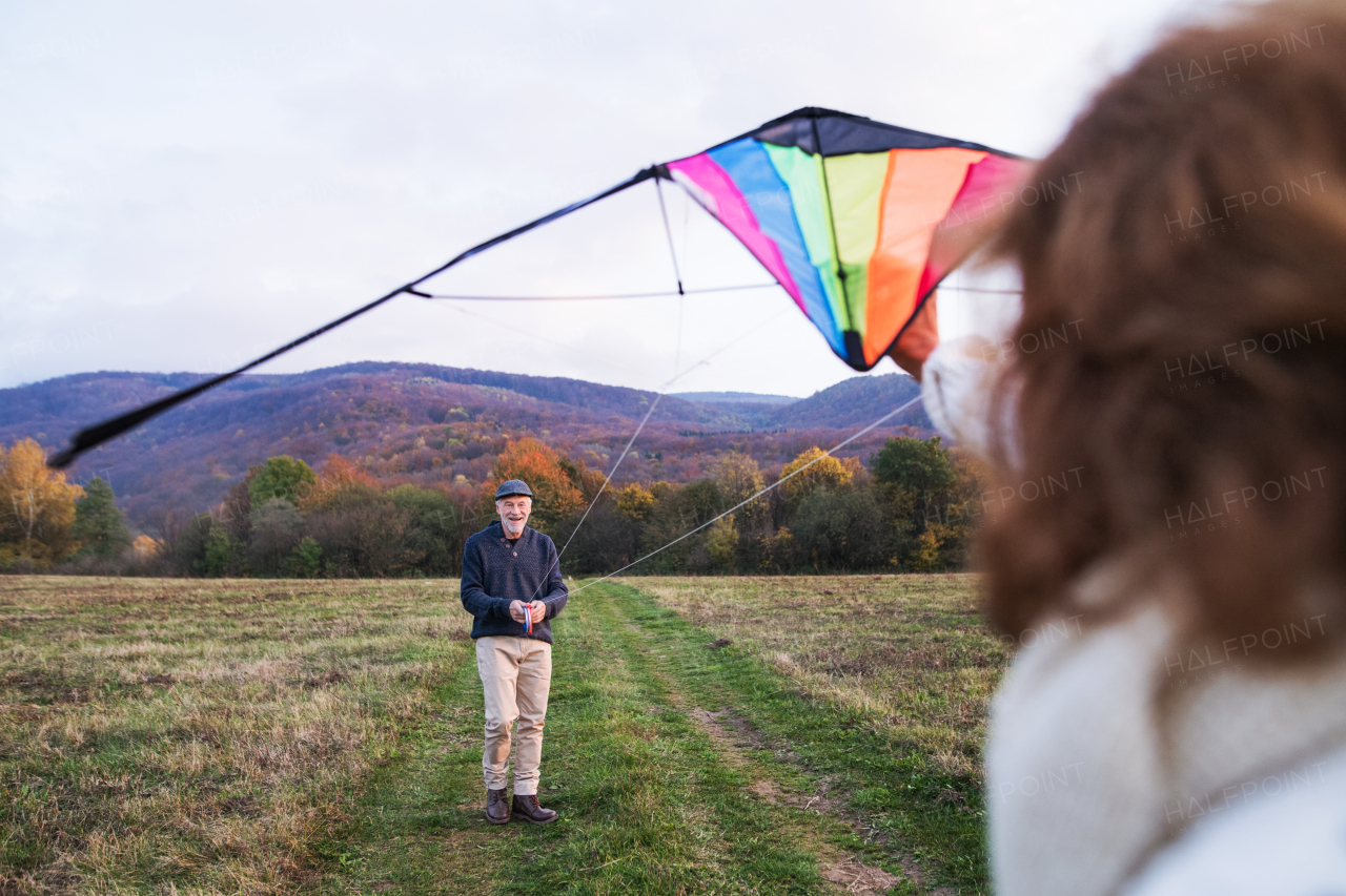 Carefree senior couple flying a colorful kite in an autumn nature.