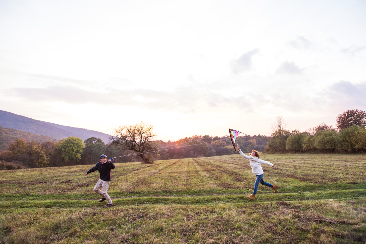 Senior couple flying a kite in an autumn nature at sunset, running. Copy space.