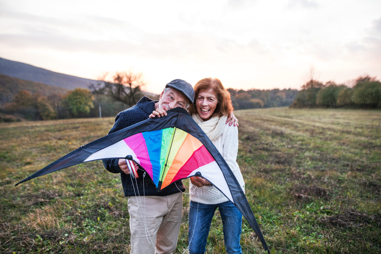 Senior man and a woman holding a kite in an autumn nature at sunset, looking at each other. Copy space.