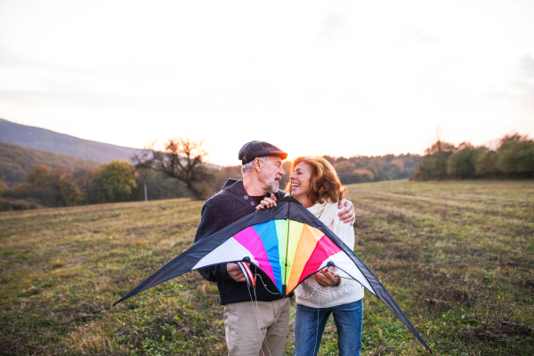 Senior man and a woman holding a kite in an autumn nature at sunset, looking at each other. Copy space.