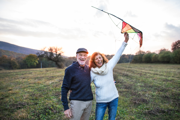 A portrait of senior man and a woman with a kite in an autumn nature at dusk time.