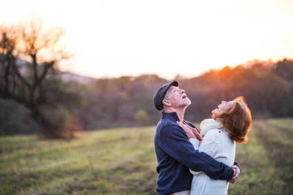 Senior couple in love on a walk in an autumn nature. Senior man and a woman hugging at sunset, looking up. Copy space.