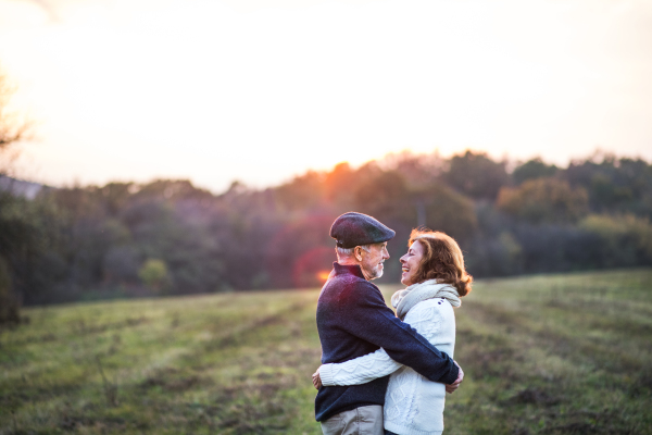 Senior couple in love on a walk in an autumn nature. Senior man and a woman hugging at sunset. Copy space.