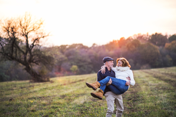 Senior couple in love on a walk in an autumn nature. Senior man carrying a woman in his arms at sunset. Copy space.