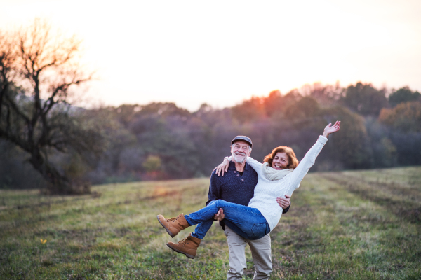 Senior couple in love on a walk in an autumn nature. Senior man carrying a woman in his arms at sunset. Copy space.