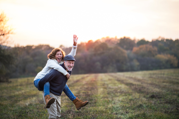 Senior man giving a woman a piggyback ride in an autumn nature. Copy space.