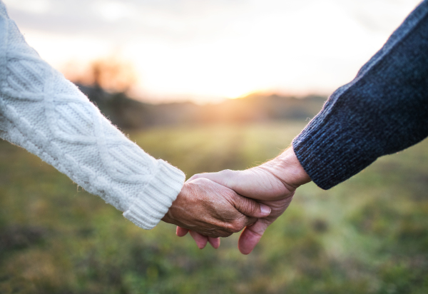 A close-up of holding hands of unrecognizable senior couple in an autumn nature at sunset.