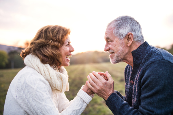 Senior couple looking at each other on a meadow in an autumn nature, holding hands.