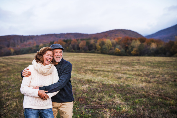 Senior couple in love on a walk in an autumn nature. Senior man and a woman hugging at sunset, laughing. Copy space.