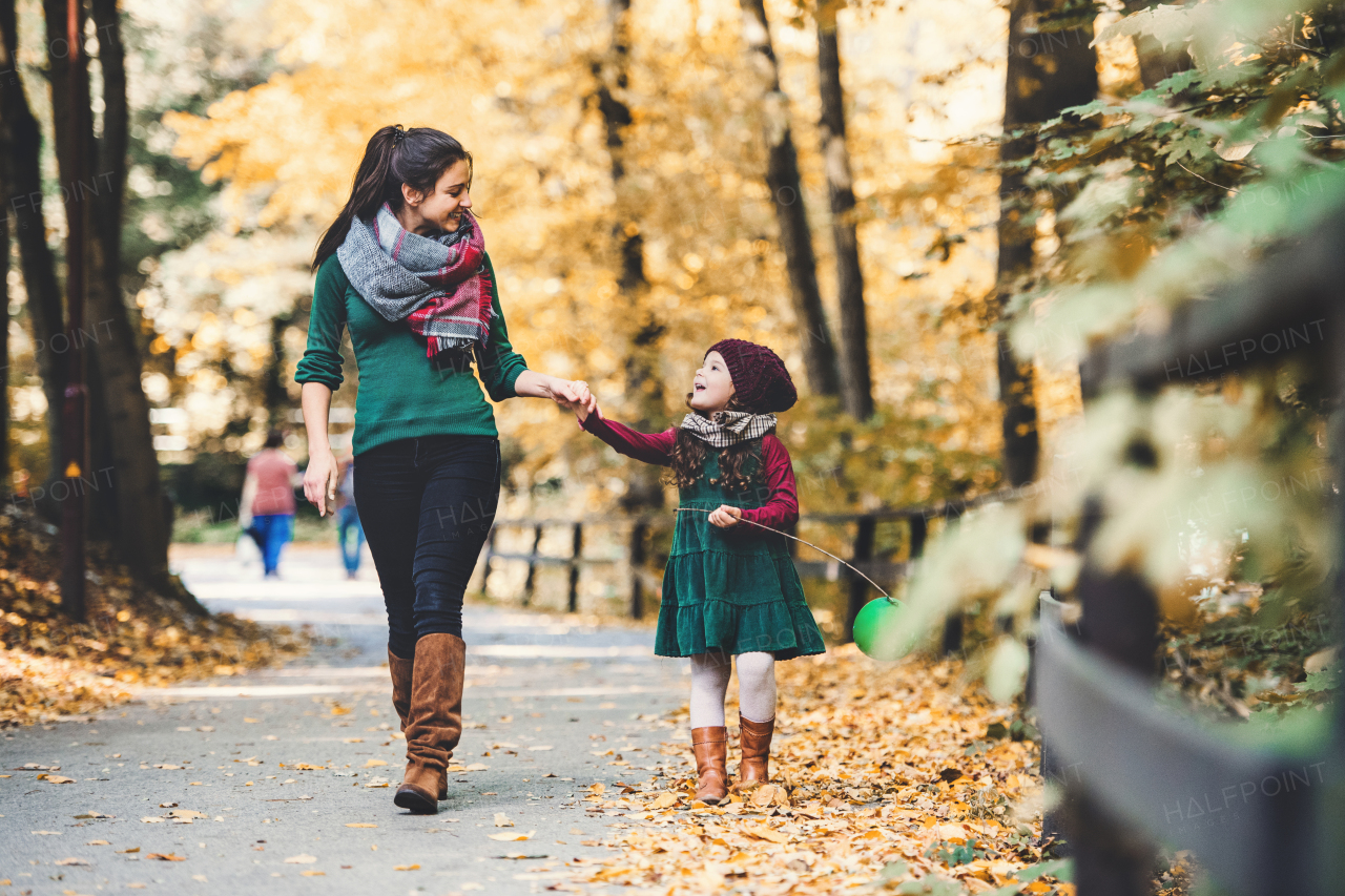 A portrait of young mother with a toddler daughter walking in forest in autumn nature, holding hands.