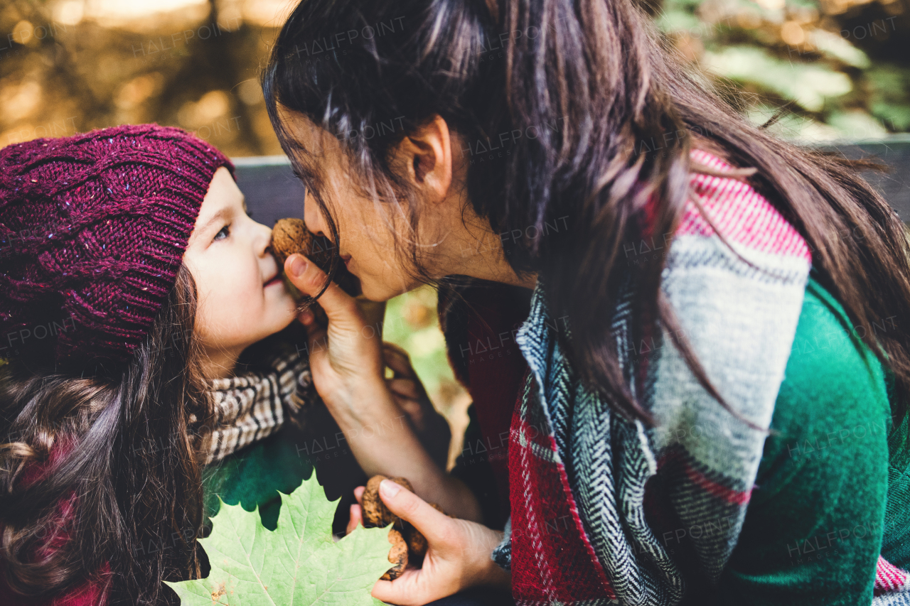 A young mother with a toddler daughter having fun with nuts in forest in autumn nature.