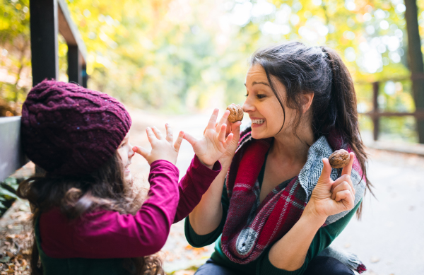 A young mother with a toddler daughter having fun with nuts in forest in autumn nature.